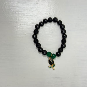Black mini bead bracelet with two green accent beads and a small gold-tone dangling charm, photographed on a light surface.
