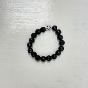 Mini black beads bracelet with a white smiley-face bead, photographed on a white surface.