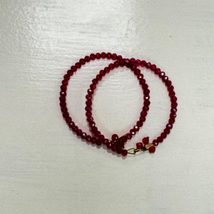 Two deep red faceted beaded bangles with gold-tone details and small red bead tassel accents, arranged on a white surface.