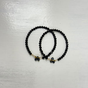Black faceted beaded bangle with delicate gold-tone details and small dangling black bead tassel accents, displayed on a white surface.
