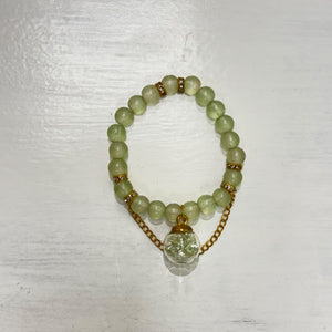 Light green beaded bracelet with gold-tone accents, delicate chain details, and a clear round charm with green decorative accents, displayed on a white surface.
