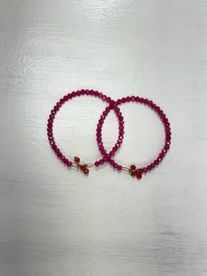 Two pink faceted beaded bangles with gold-tone details and small red decorative tassel accents, displayed on a white surface.
