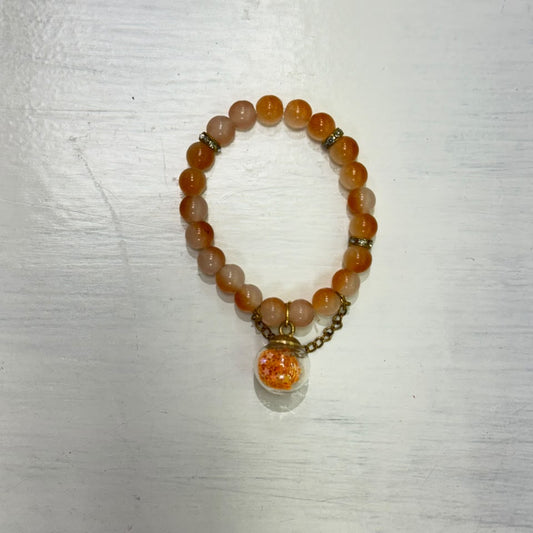 Orange and peach beaded bracelet with gold-tone accents and a round decorative pendant charm, displayed on a white surface.