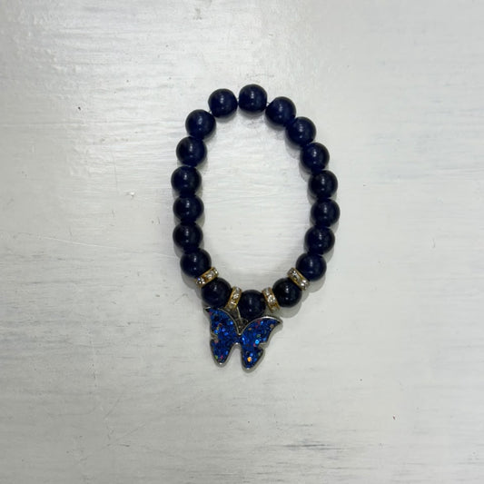 Dark beaded bracelet with gold-tone spacer beads and a sparkling blue butterfly charm, photographed on a light surface.